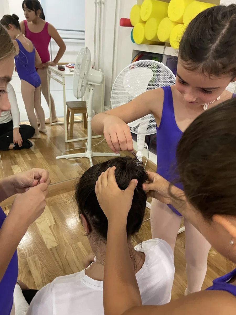 Varias alumnas con maillot morado haciendo entre todas el moño a una compañera sentada en el suelo de la sala