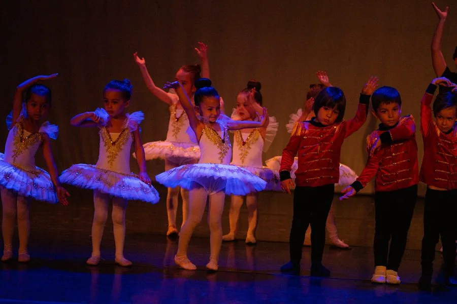 Fila de peques en el escenario, unas con tutú blanco y otros con casaca roja, bajo una luz azul durante el festival de In Stage