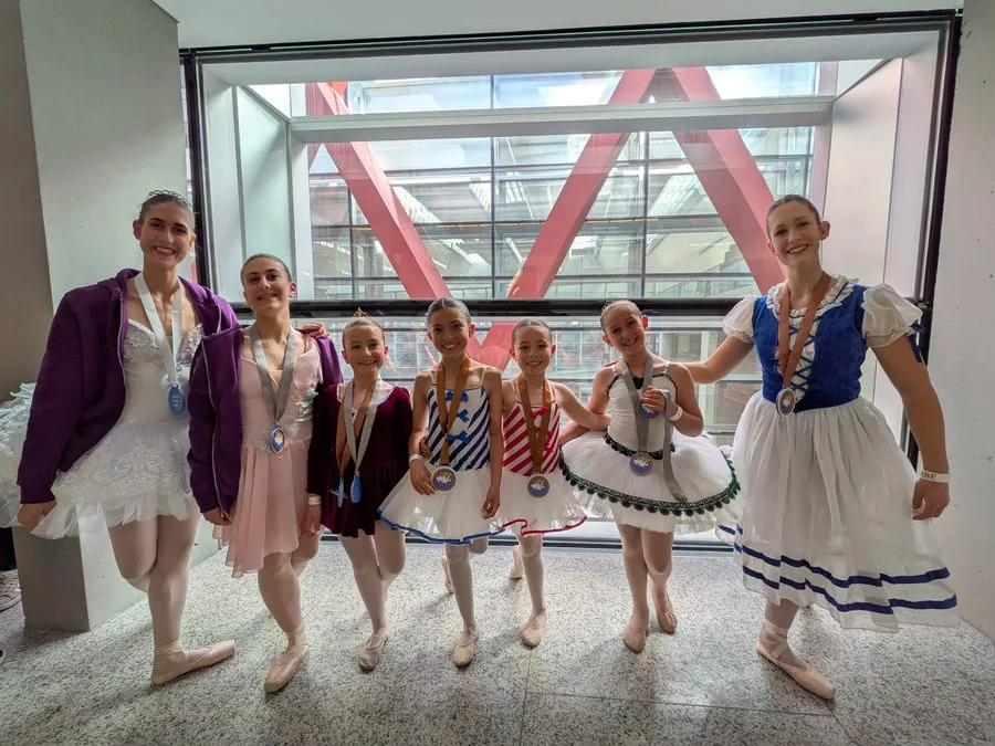 Siete alumnas de In Stage con tutús de colores y las medallas del concurso Orbe al cuello, en el vestíbulo acristalado del certamen